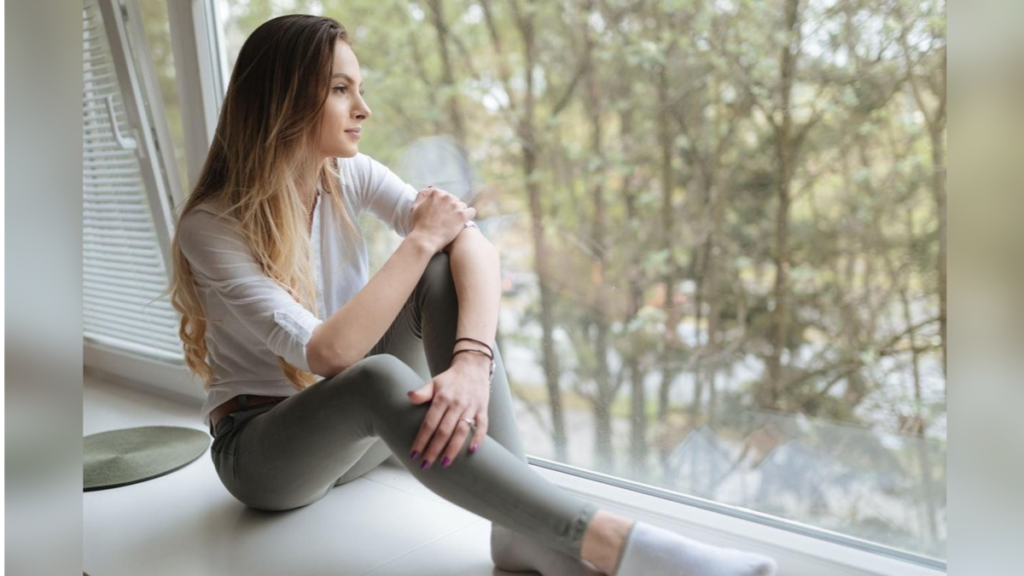 Corrê Viva Saudável 1 Mulher sentada perto da janela observando a natureza, transmitindo sensação de calma, reflexão e bem-estar.